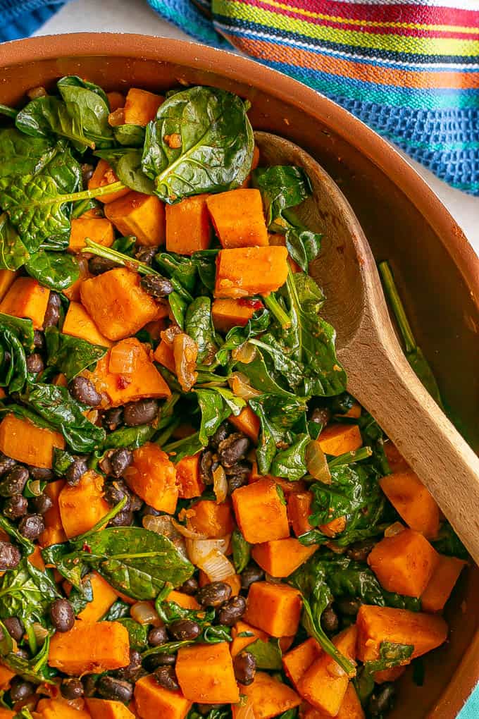 Close up of a copper skillet with sweet potatoes, black beans and wilted spinach