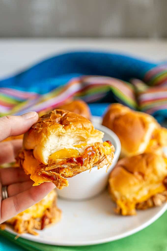 A hand holding up a cheesy BBQ chicken slider roll