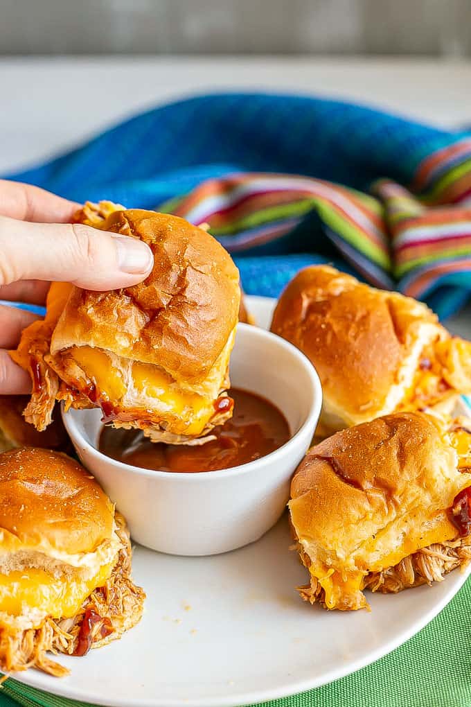 A hand dipping a cheesy BBQ chicken slider roll into BBQ sauce