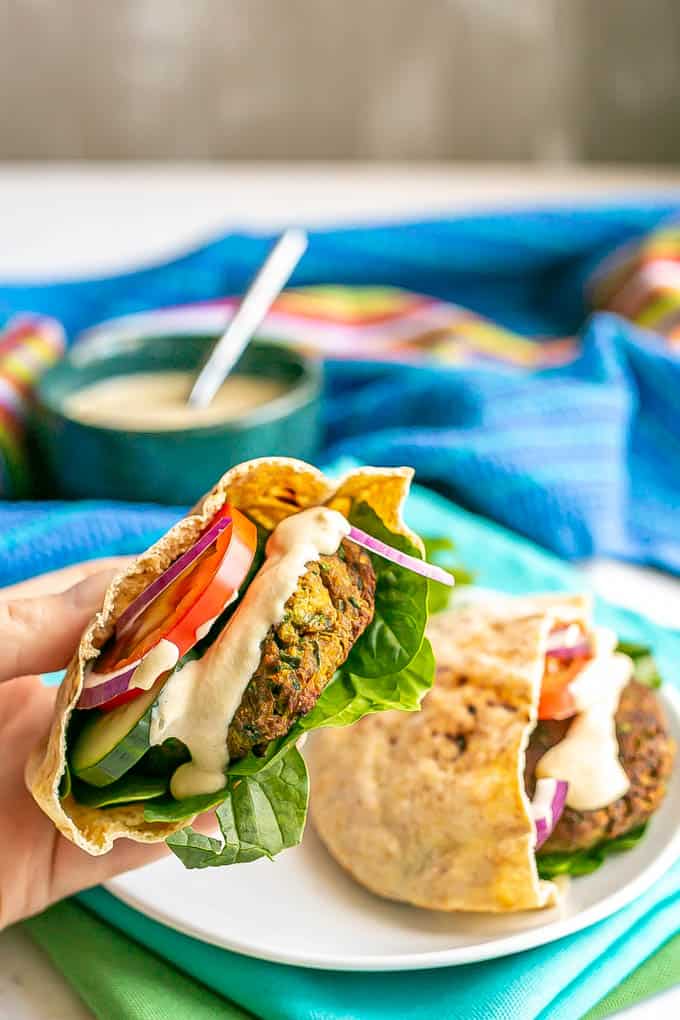 A hand holding up a pita stuffed with baked falafel, lettuce, tomato, cucumber, red onion and tahini sauce