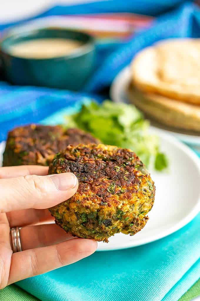 A hand holding up a small browned falafel patty