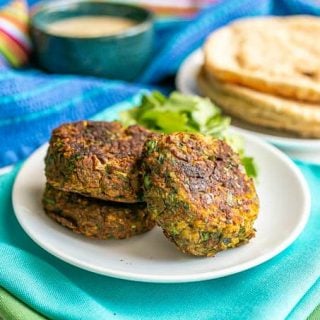 A trio of baked falafel patties on a white plate with pita bread in the background