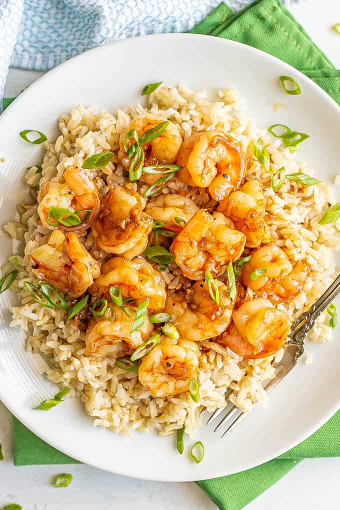 Honey garlic shrimp piled over some steamed brown rice on a white plate, topped with sliced green onions