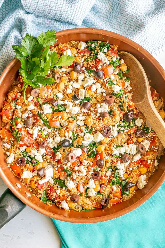 Quinoa and chickpea mix in a copper skillet with tomatoes and spinach with feta cheese and olives on top
