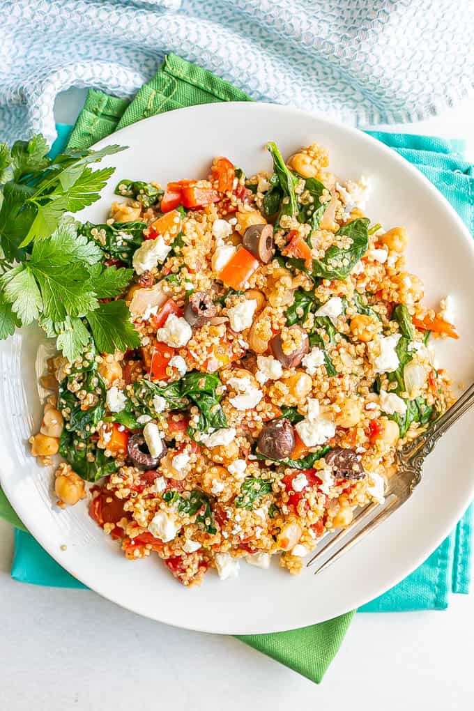 A white dinner plate of a vegetarian quinoa mix with chickpeas, spinach and tomatoes with a fork alongside
