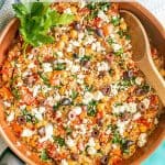 Quinoa and chickpea mix in a copper skillet with tomatoes and spinach with feta cheese and olives on top and a text overlay on the photo