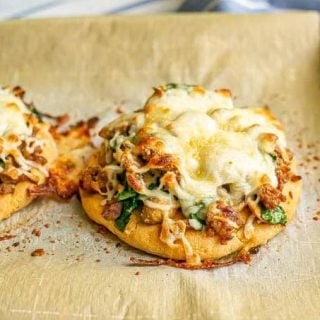 Two cheesy sausage and veggie flatbreads on a parchment paper lined baking sheet after being baked