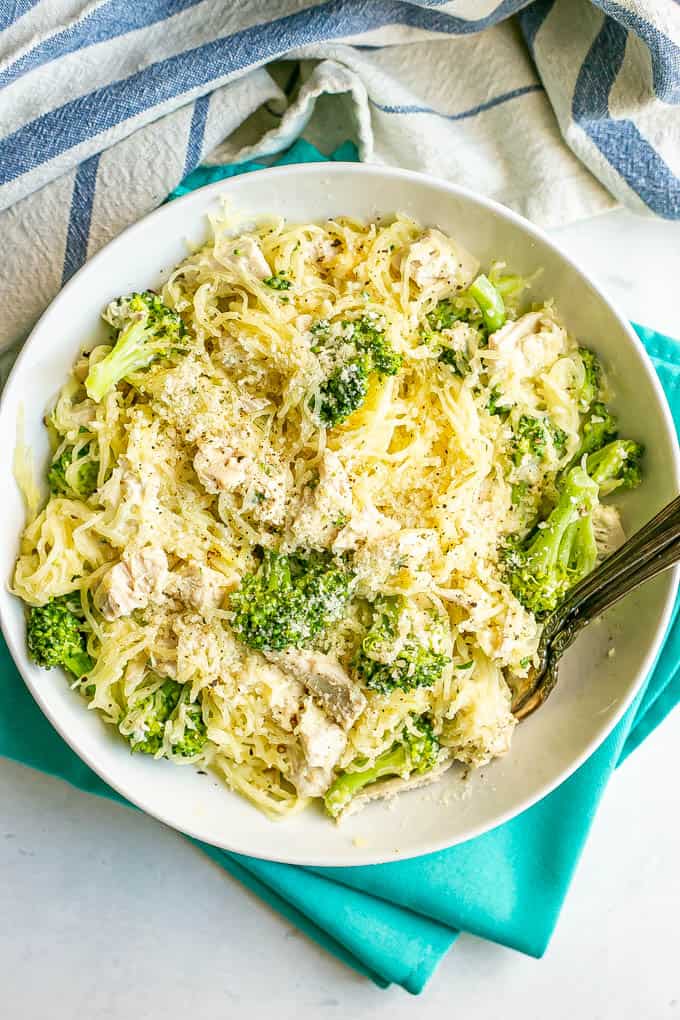 A white dinner bowl with spaghetti squash, chicken and broccoli topped with grated Parmesan cheese