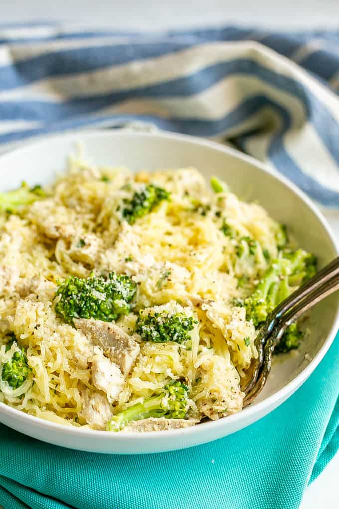 A white dinner bowl filled with spaghetti squash mixed with chicken and broccoli and topped with Parmesan cheese with two forks resting in the bowl
