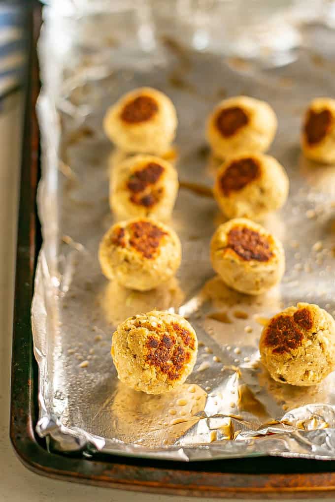 Rows of cooked small meatballs on a foil lined baking sheet