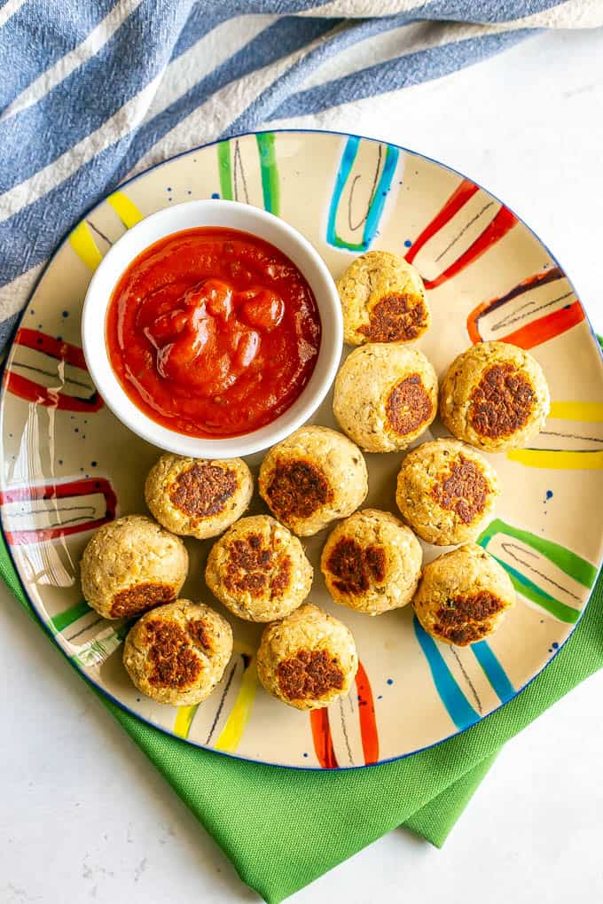 A dozen small baby meatballs on a colorful plate with a little bowl of marinara sauce