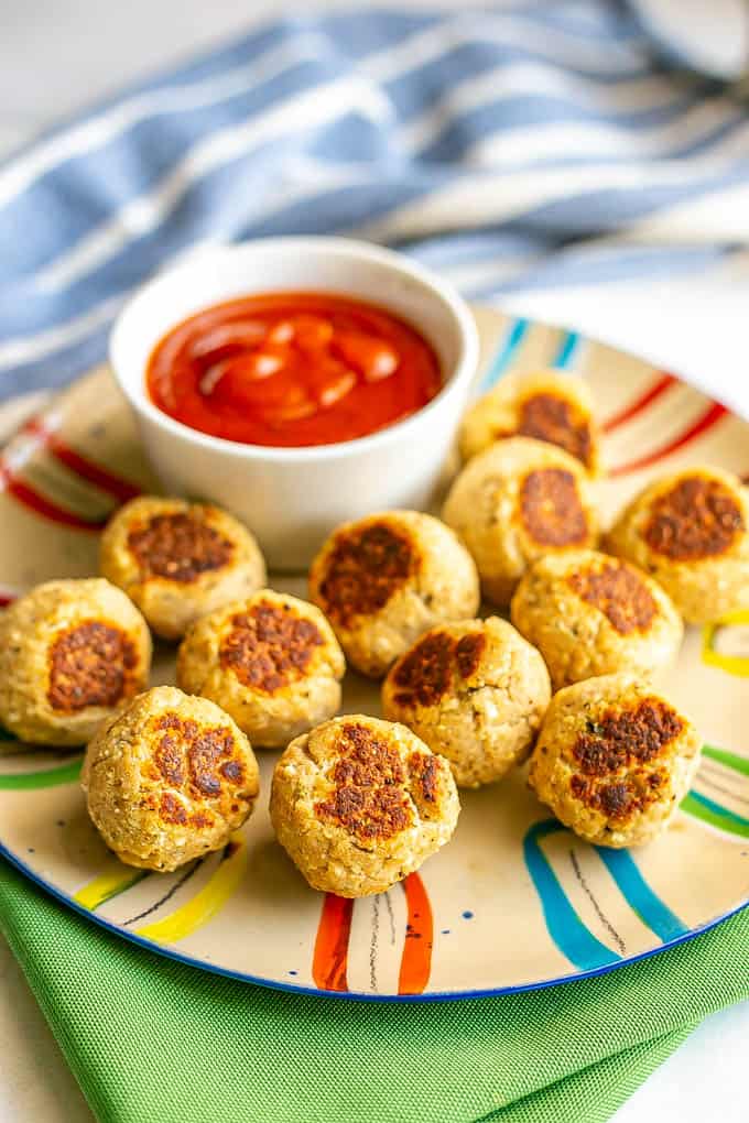 A dozen small, browned baby meatballs on a colorful plate with a little bowl of marinara sauce