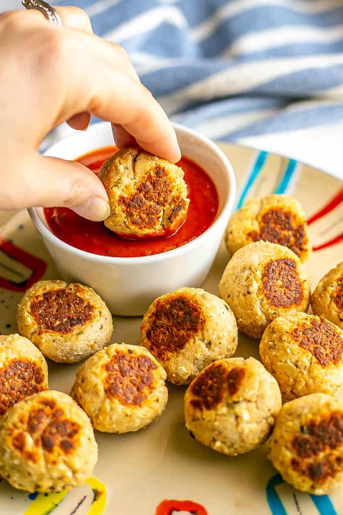 A hand dipping a small turkey meatball into a white dish of marinara sauce