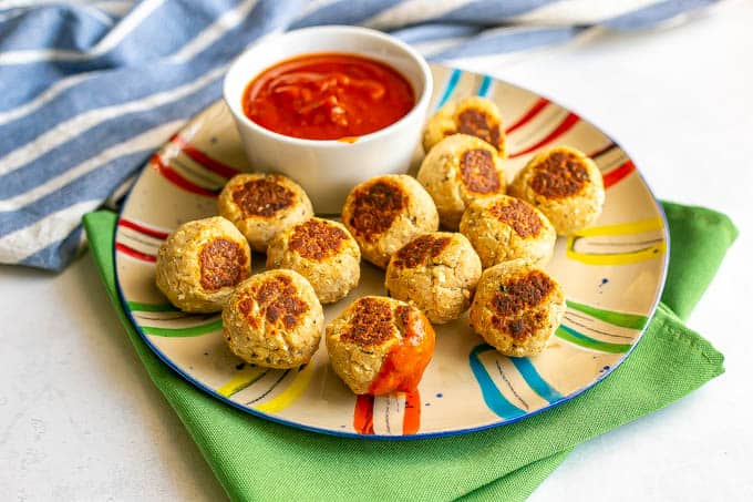 A dozen small baby meatballs on a colorful plate with a little bowl of marinara sauce and one meatball dipped in it