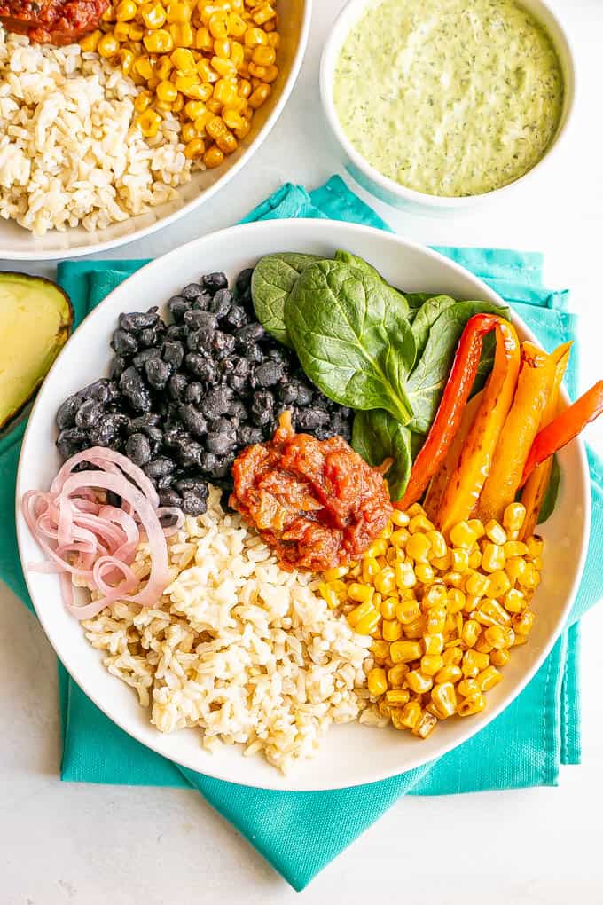 Close up of a vegetarian rice bowl with beans and vegetables with a bowl of green dressing nearby