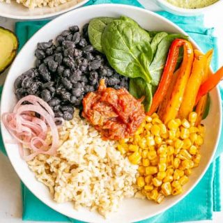 An arranged vegetarian power bowl with beans, rice, veggies, salsa and a halved avocado beside the plate
