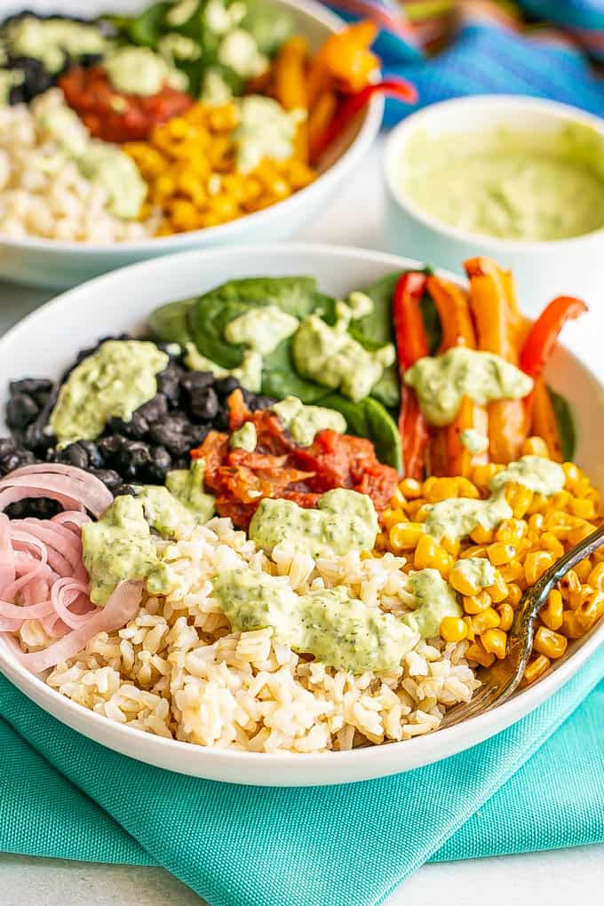 A fork resting in a large white bowl with rice, beans, veggies and toppings