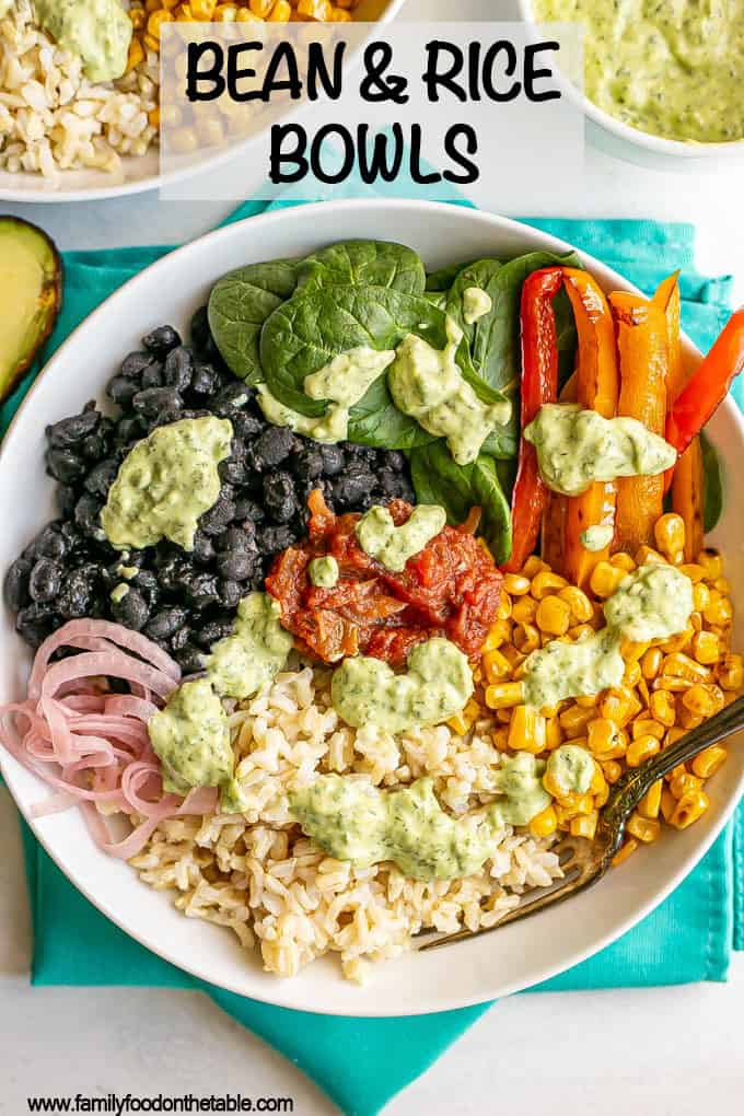 A large white bowl with brown rice, black beans, spinach, peppers and corn, plus a cilantro lime dressing drizzled over top and a text overlay on the photo