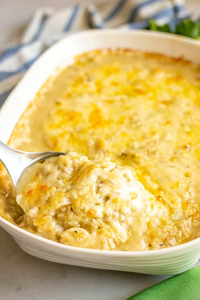 A metal spoon scooping up some chicken and rice casserole from a large white baking dish