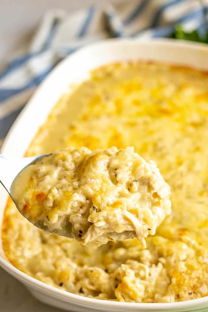 A metal spoon lifting up a scoop of chicken and rice casserole from a large white baking dish