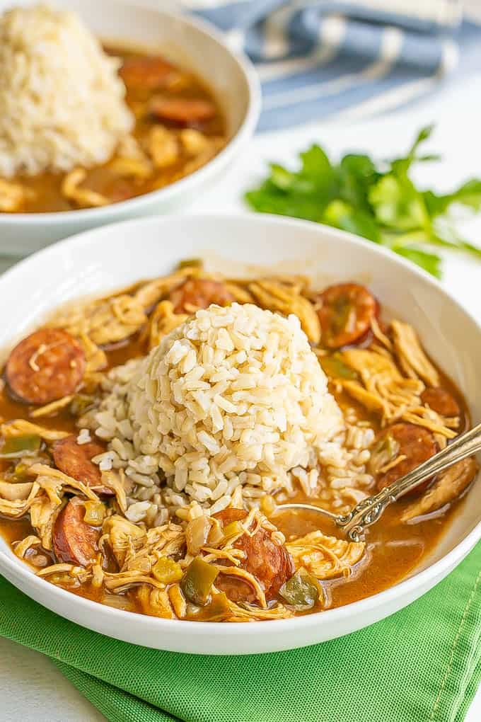 Chicken and sausage gumbo served in a wide low white bowl with a pile of rice in the middle and a spoon resting in the bowl