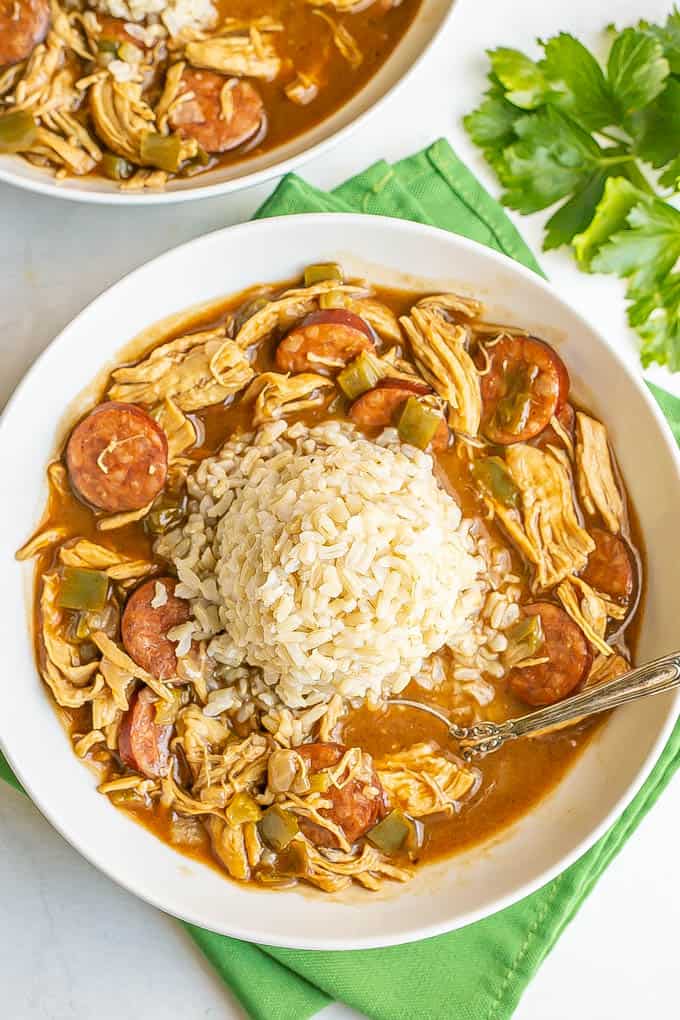 Chicken and sausage gumbo served in a wide low white bowl with a pile of rice in the middle and a spoon resting in the bowl