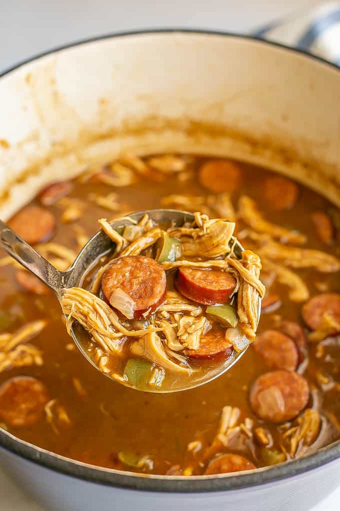 A ladle scooping up some chicken gumbo from a large purple pot