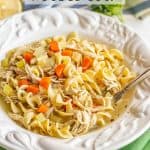 A white soup bowl with details on the rim filled with chicken noodle soup and a spoon resting to the side with a text overlay on the photo