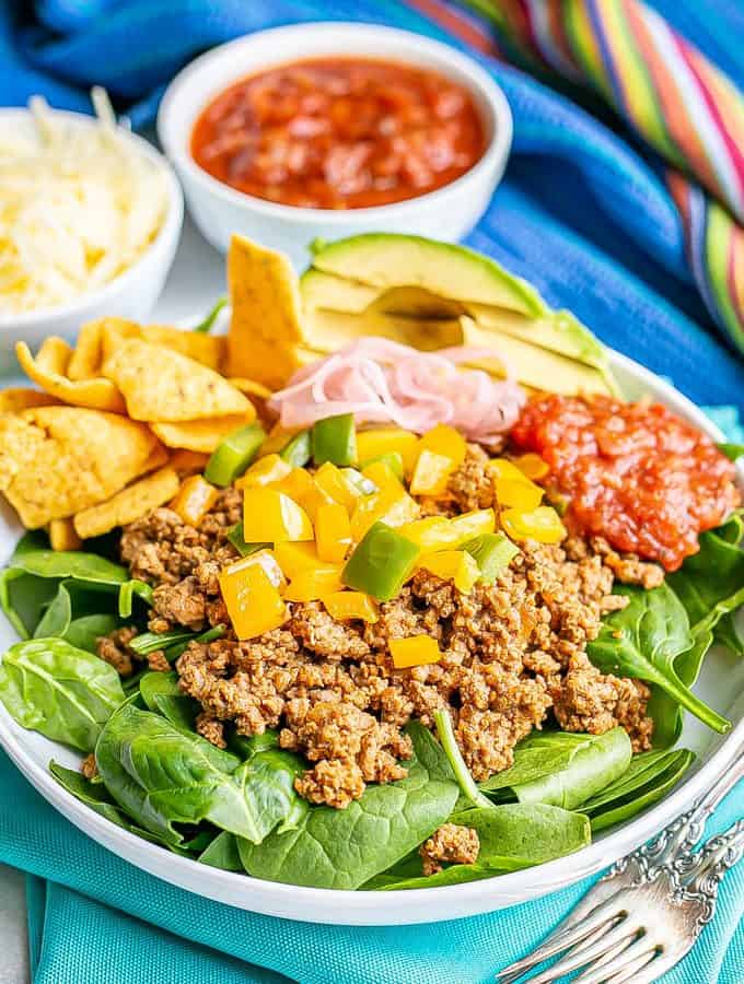 Ground taco meat with peppers piled on a bed of lettuce in a large shallow white bowl with toppings to the side