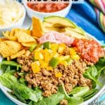 Ground taco meat with peppers piled on a bed of lettuce in a large shallow white bowl with toppings to the side and a text overlay on the photo