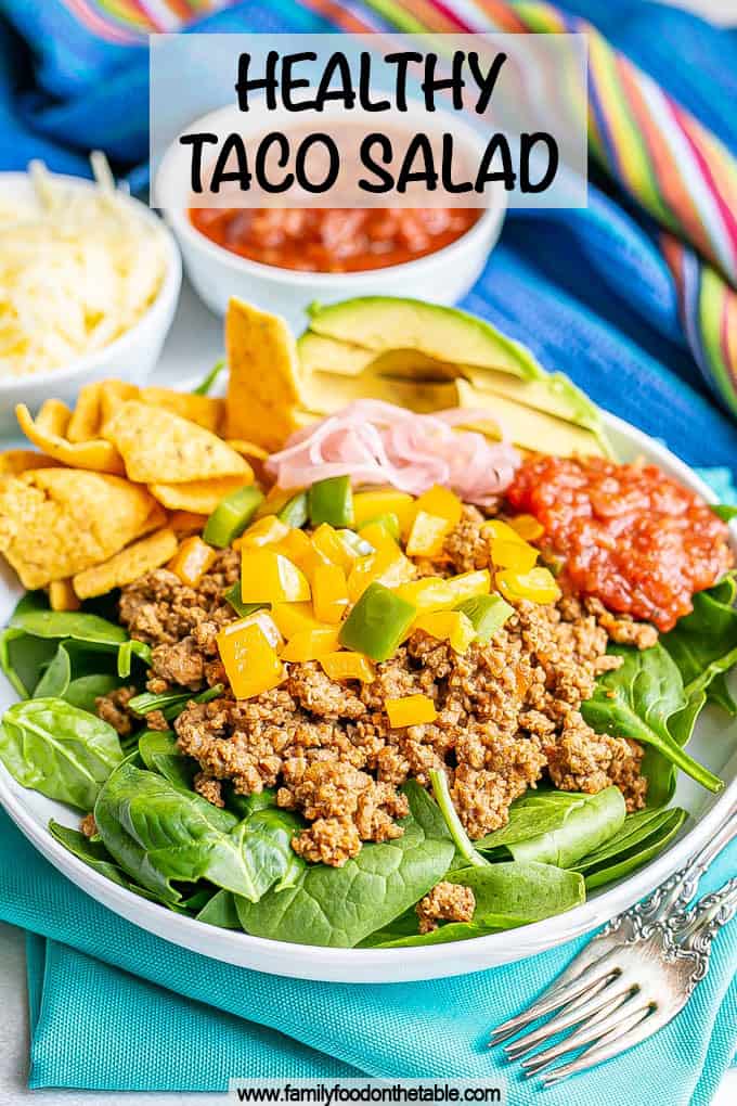Ground taco meat with peppers piled on a bed of lettuce in a large shallow white bowl with toppings to the side and a text overlay on the photo