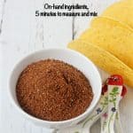 A bowl of homemade taco seasoning spice mixture with measuring spoons and taco shells nearby