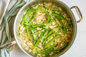 Sauteed onions and green bell peppers in a large all-clad skillet