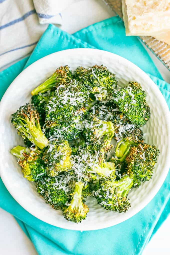 A white bowl full of browned and crispy broccoli florets with fresh Parmesan cheese grated over top