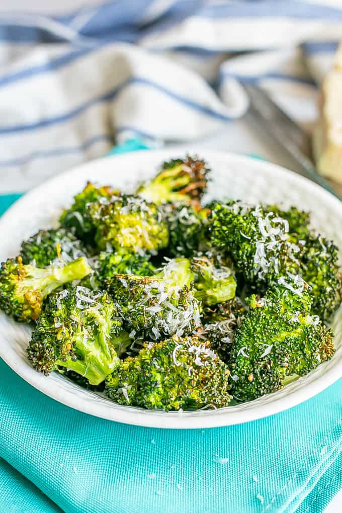 A white bowl full of browned Air Fryer broccoli florets with fresh Parmesan cheese grated over top