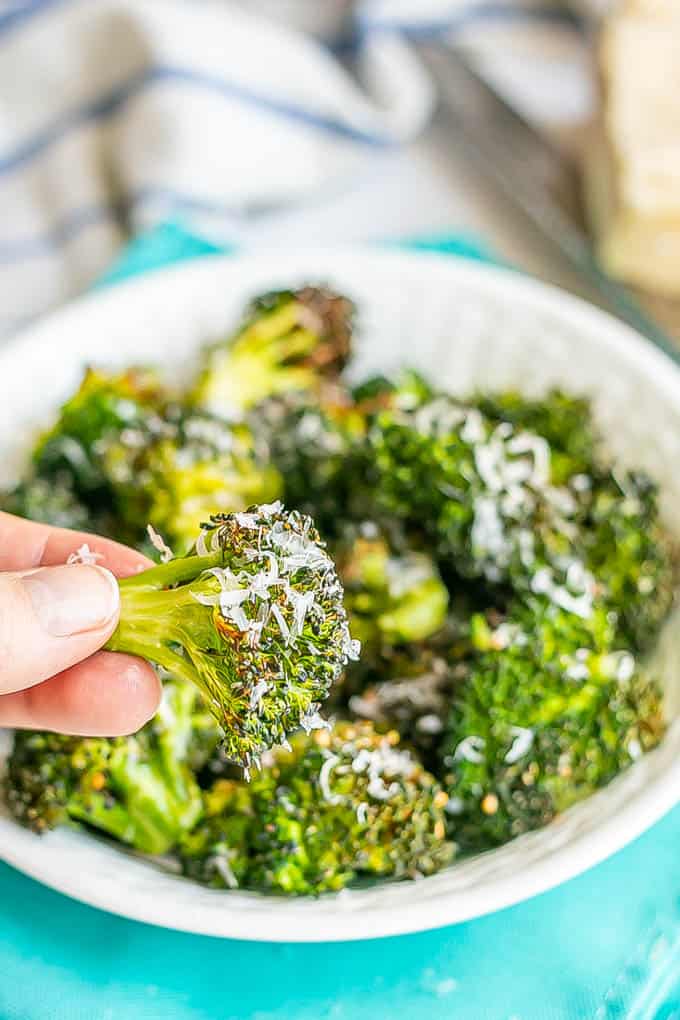 A hand holding a crispy Air Fryer broccoli floret with Parmesan cheese grated on it