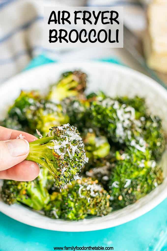 A hand holding a crispy Air Fryer broccoli floret with Parmesan cheese grated on it and a text overlay on the image