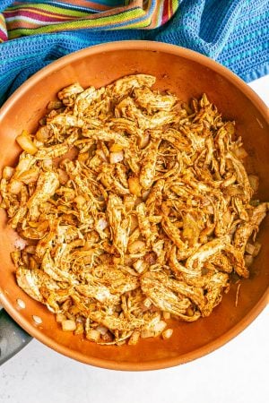 A large skillet with taco seasoned shredded chicken