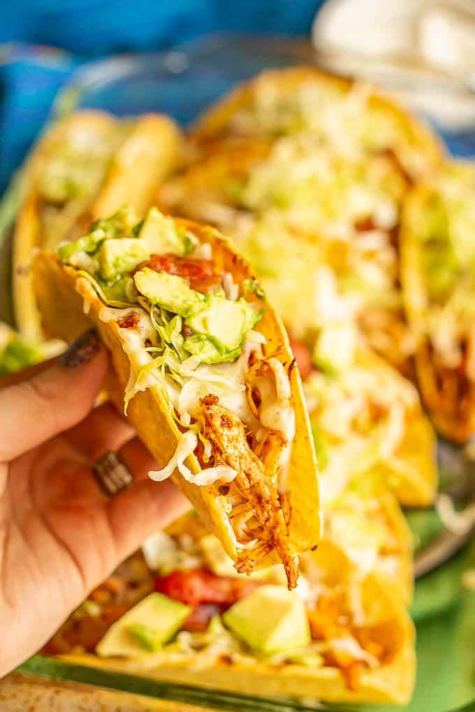 A hand holding up a baked shredded chicken crispy taco with salsa and avocado on top