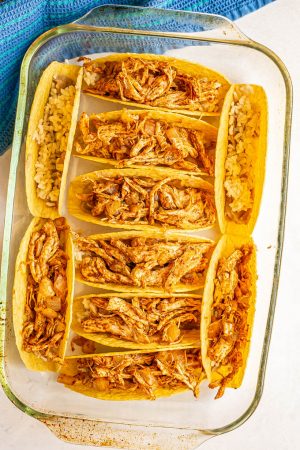 A pan of taco shells with refried beans, rice and shredded chicken, before being baked