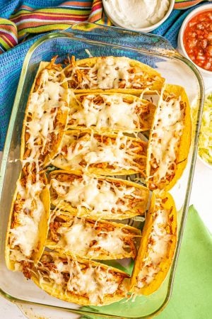 A pan of cheesy shredded chicken tacos in a casserole dish after being baked, with bowls of toppings nearby