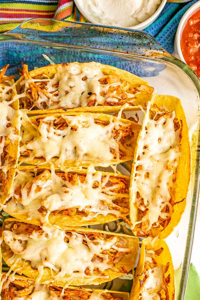 Cheesy shredded chicken tacos in a casserole dish after being baked, with bowls of toppings nearby