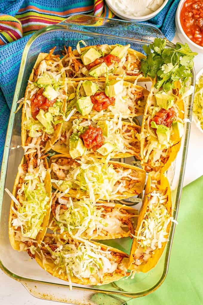 A casserole dish full of stuffed chicken tacos after being baked and with toppings added