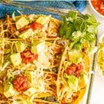 Baked shredded chicken tacos in a glass baking dish with avocado and salsa for toppings and a text overlay on the photo.