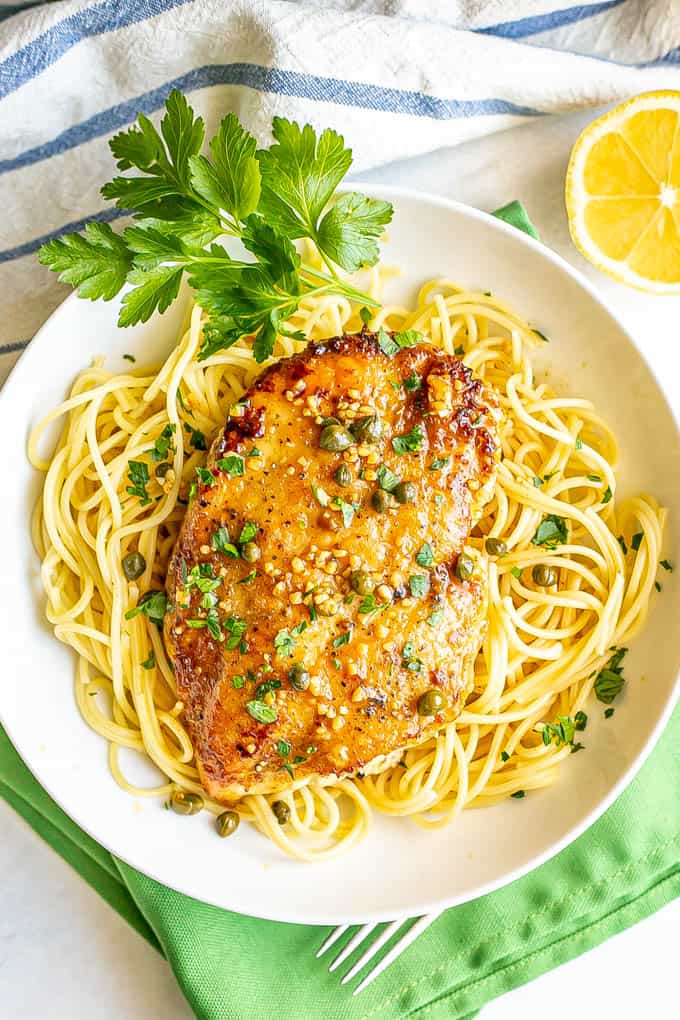 Easy lemon chicken piccata served with a garlic caper white wine sauce over spaghetti noodles in a large white bowl