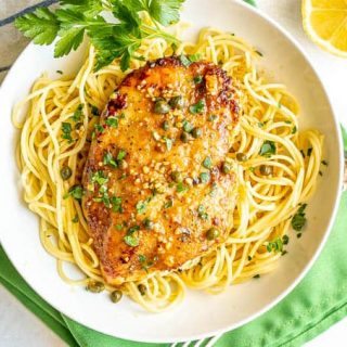 Overhead shot of chicken piccata served over thin spaghetti noodles in a low shallow white bowl with parsley sprinkled on top