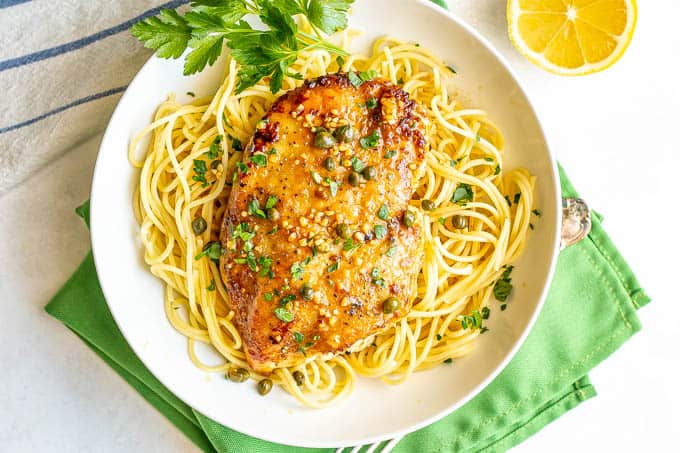 Overhead shot of chicken piccata served over thin spaghetti noodles in a low shallow white bowl with parsley sprinkled on top