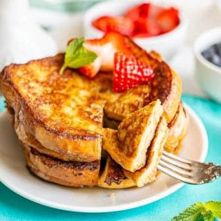 A fork picking up a cut out slice of French toast from a stack on a small white plate