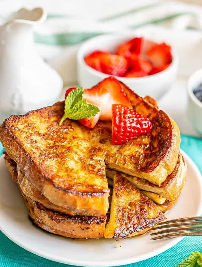 Stacked slices of French toast on a plate with berries on top and a small bite cut out