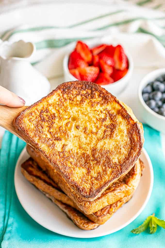 A slice of French toast being added to a stack on a plate